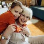 Happy little girl having fun while embracing her grandmother at home.